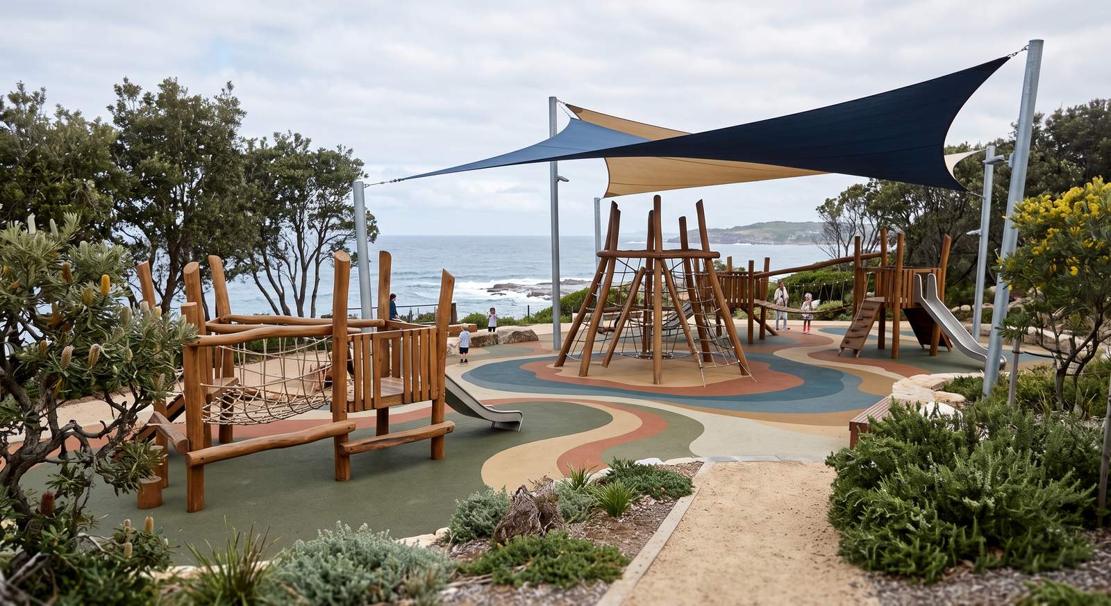 A coastal play space with timber climbing structures, coloured surfacing and shade sails